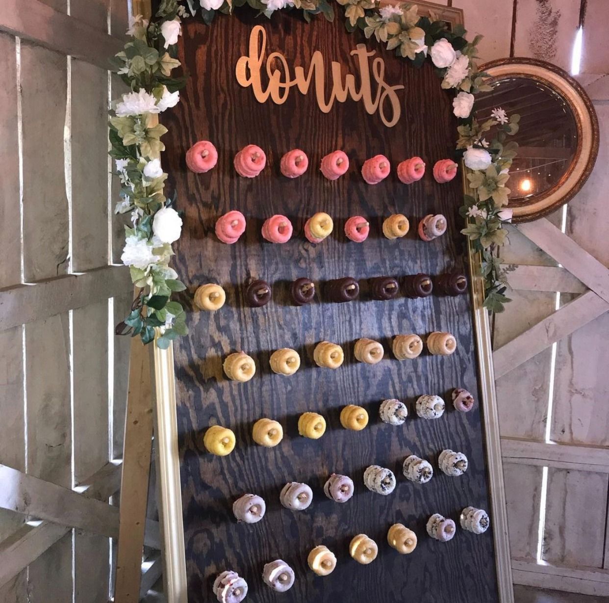 Donuts display board with rows of pink, yellow, and white frosted donuts under a “donuts” sign