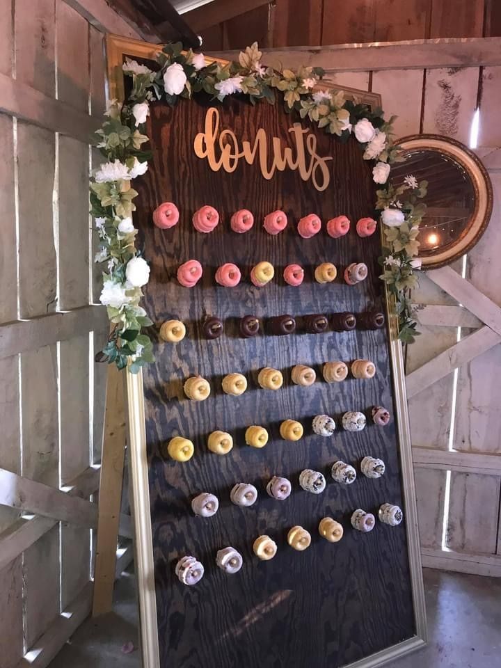 Floral donut wall display with rows of pink, yellow, and white donuts on a black board in a rustic setting