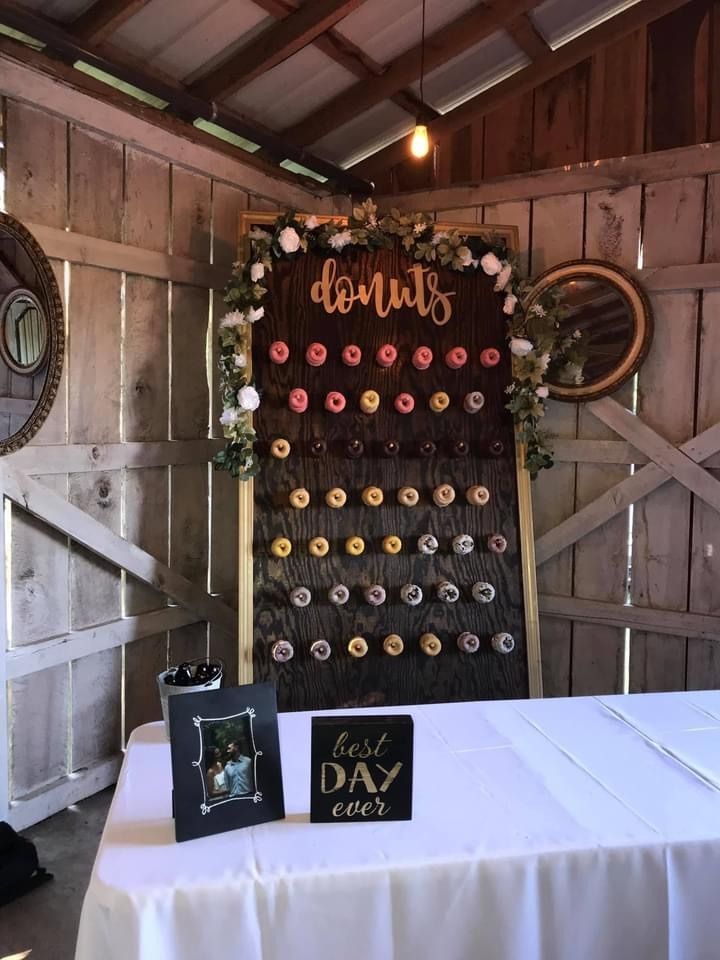 Donuts display with black backdrop and colorful donut wall in rustic barn venue with white tablecloth and signage