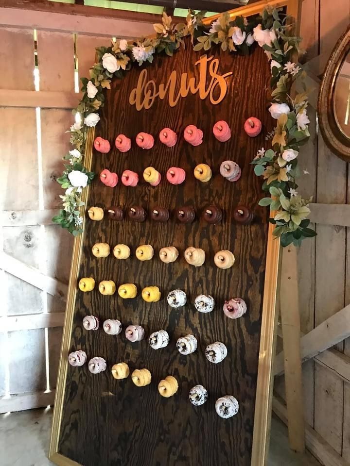 Donuts displayed on a rustic wooden board with flowers, arranged in rows at a party or event table