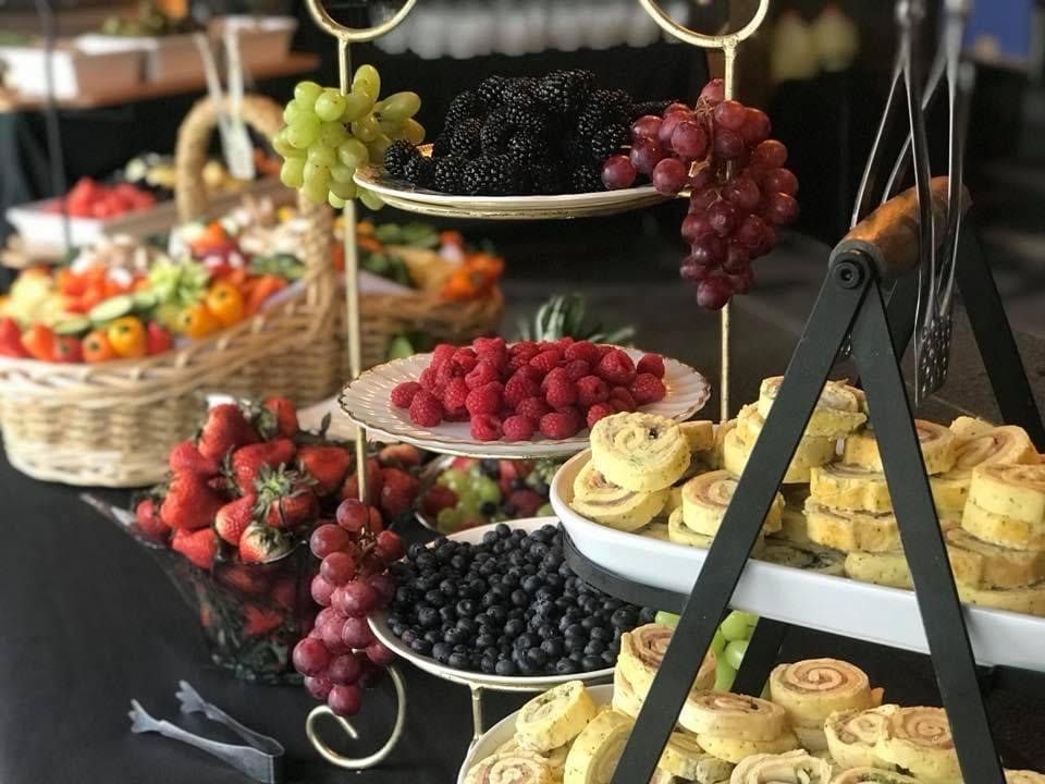 Tiered trays of fresh fruit and pastries on a buffet table, with berries, grapes, and rolled cakes.