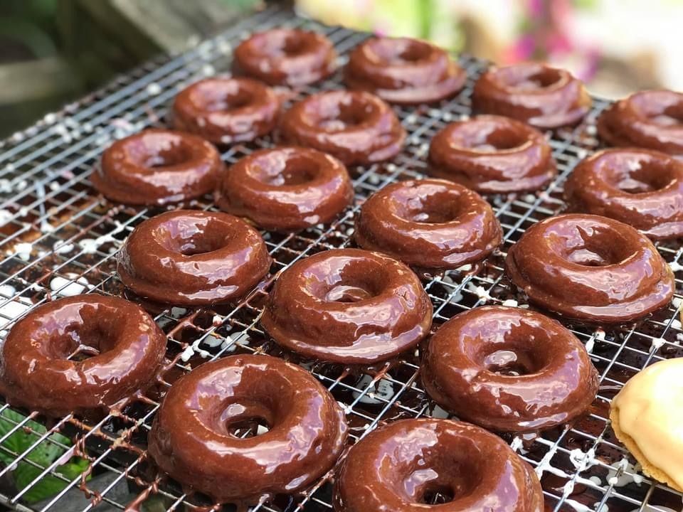 Chocolate-glazed donuts cooling on a wire rack, with one plain donut at the edge