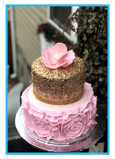 Two-tier pink and gold cake with ruffled frosting and a pink flower topper on a stand