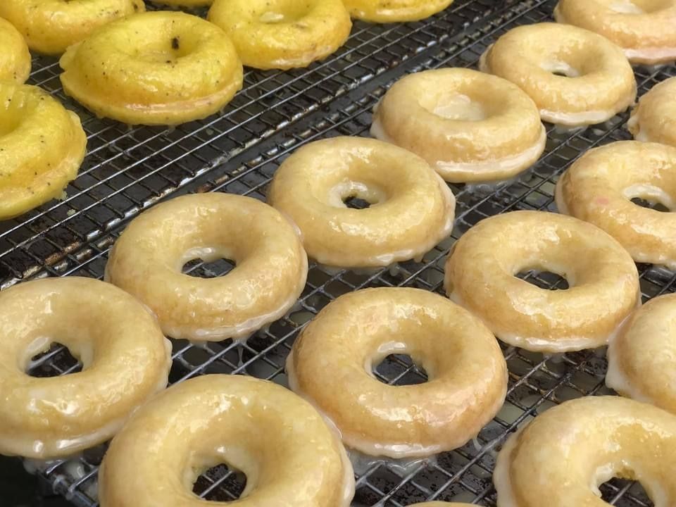 Rows of glazed donuts cooling on wire racks, some golden and some lightly browned.