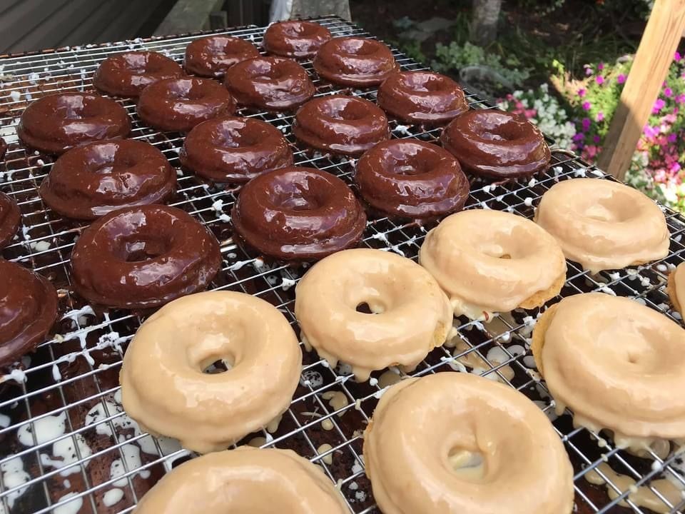 Rows of chocolate and glazed donuts cooling on a wire rack at an outdoor market stall