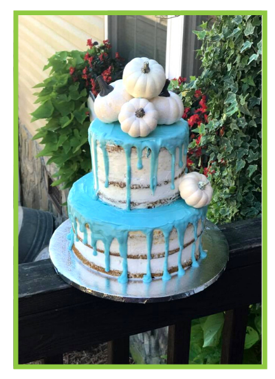 Blue two-tier cake with white frosting and flowers, displayed outdoors on a stand.