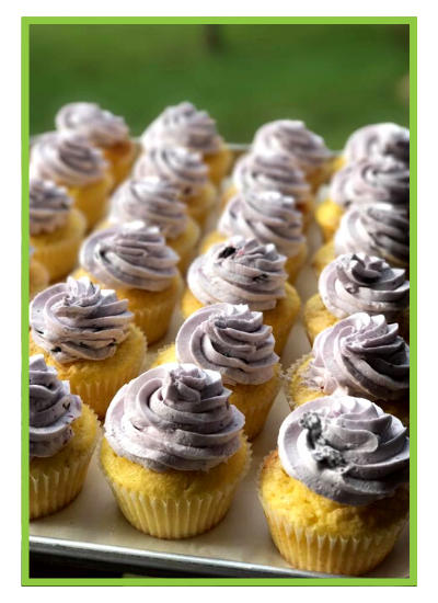 Cupcakes with lavender frosting on a tray, arranged in neat rows against a green background