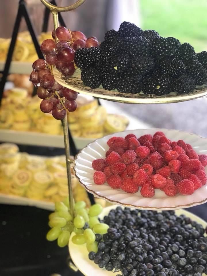 Tiered trays of blackberries, raspberries, blueberries, green grapes, and red grapes at a fruit display