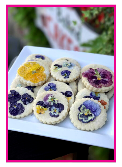 White plate with six flower-shaped shortbread cookies topped with colorful dried petals.