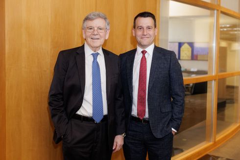 Two men in suits and ties are standing next to each other in a hallway.