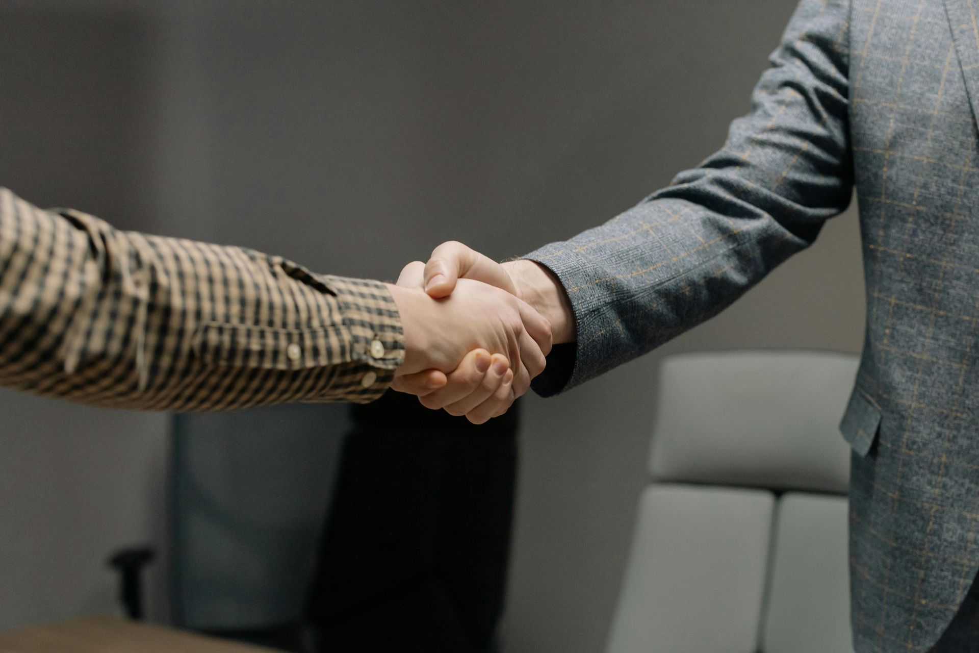 A man in a suit is shaking hands with another man in a plaid shirt.