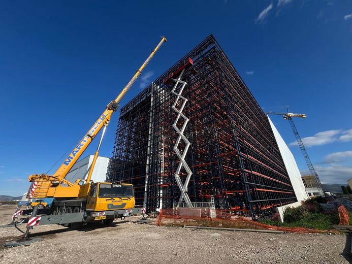 Cantiere edile con un edificio nero sotto impalcature e una gru gialla sullo sfondo di un cielo azzurro.