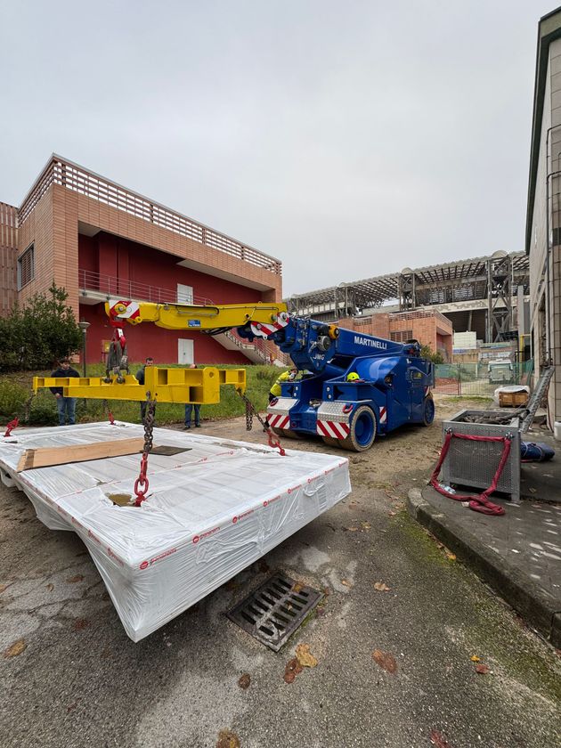 Ampio capannone industriale con una gru a ponte gialla, un carrello elevatore, operai e attrezzature sul pavimento.