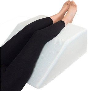Piernas apoyadas sobre un cojín blanco en forma de cuña, con leggings negros y pies descalzos.