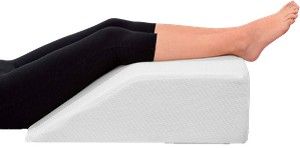 Piernas apoyadas sobre un cojín blanco en forma de cuña, con leggings negros y pies descalzos.