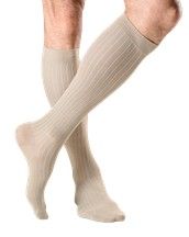 Un par de calcetines de compresión beige hasta la rodilla en las piernas cruzadas.