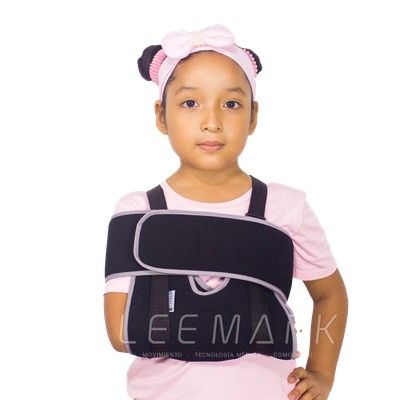 Niño con cabestrillo negro y camisa blanca, sonriendo sobre un fondo blanco.