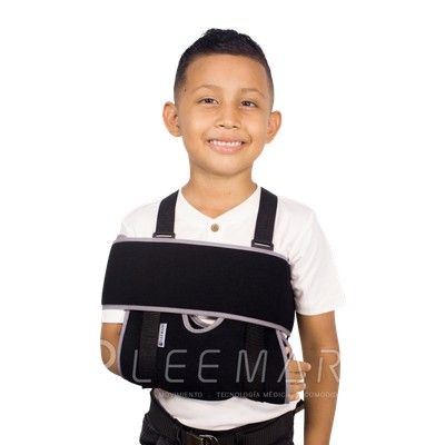 Niño con cabestrillo negro y camisa blanca, sonriendo sobre un fondo blanco.