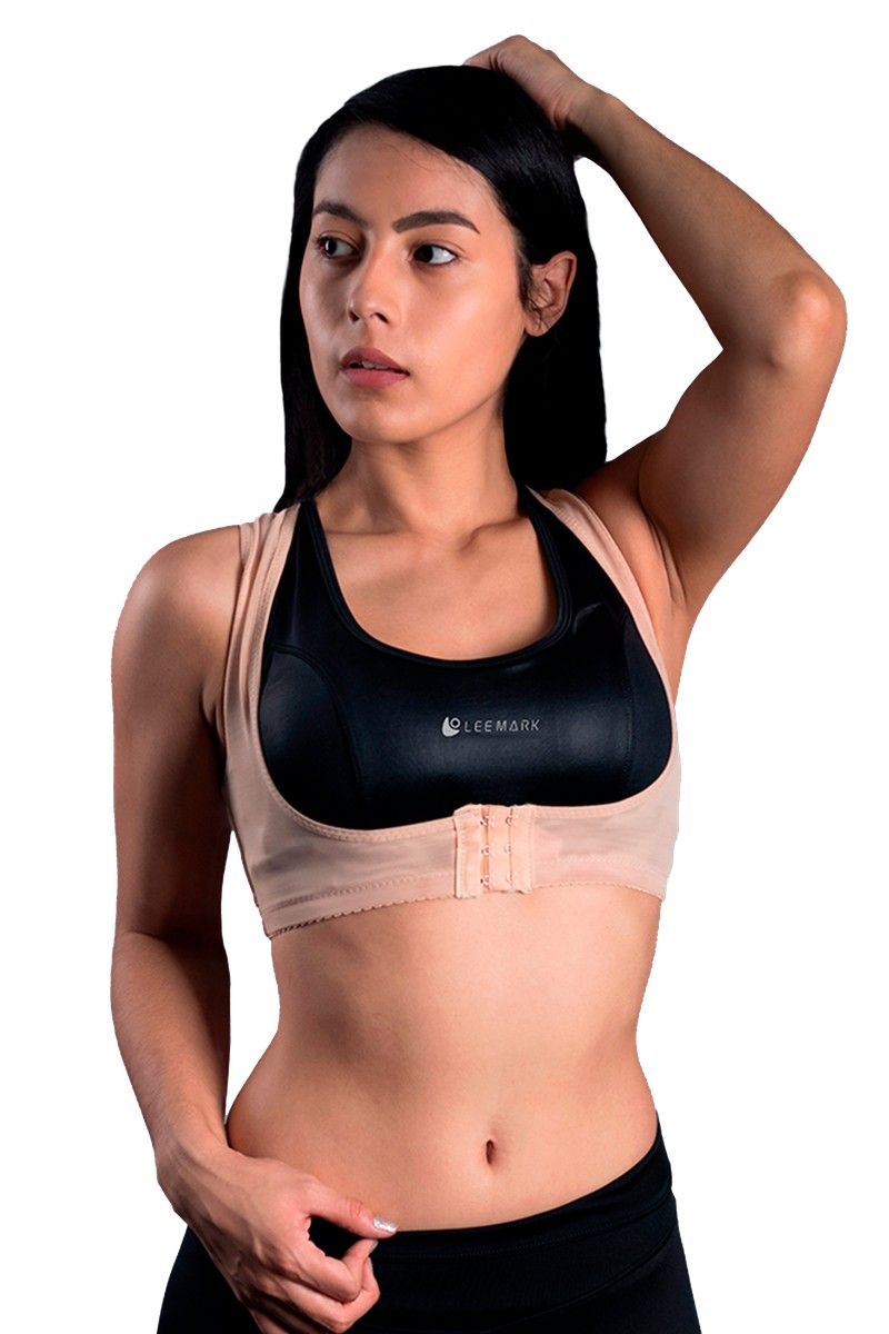 Mujer con sujetador deportivo beige y mallas negras, vista de espaldas sobre fondo blanco.
