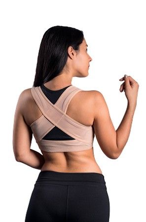 Mujer con sujetador deportivo beige y mallas negras, vista de espaldas sobre fondo blanco.