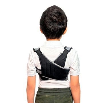 Niño con un corrector postural gris sobre una camisa polo blanca sobre un fondo liso.