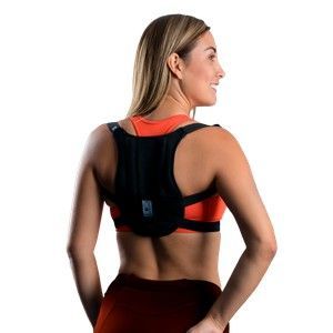 Mujer con un corrector postural negro sobre una camiseta deportiva roja, vista de espaldas sobre un fondo blanco.