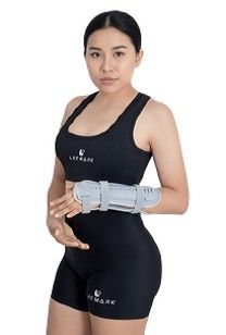 Mujer con ropa deportiva negra y muñequeras grises sobre un fondo blanco.