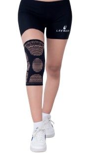 Persona con pantalones cortos negros y una rodillera negra, de pie con zapatillas blancas sobre un fondo blanco liso.