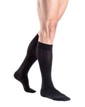 Piernas de la persona con medias de compresión negras hasta la rodilla y calcetines negros.