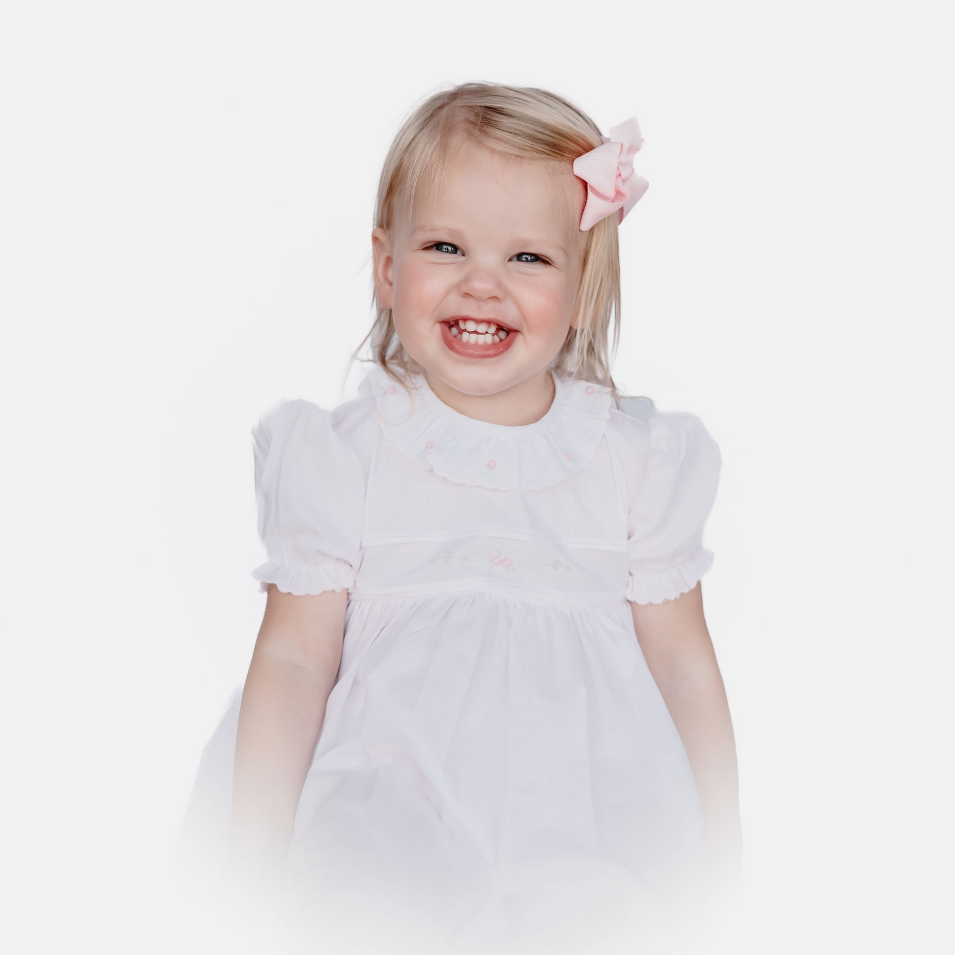 Smiling child in a white dress with a pink bow against a white background