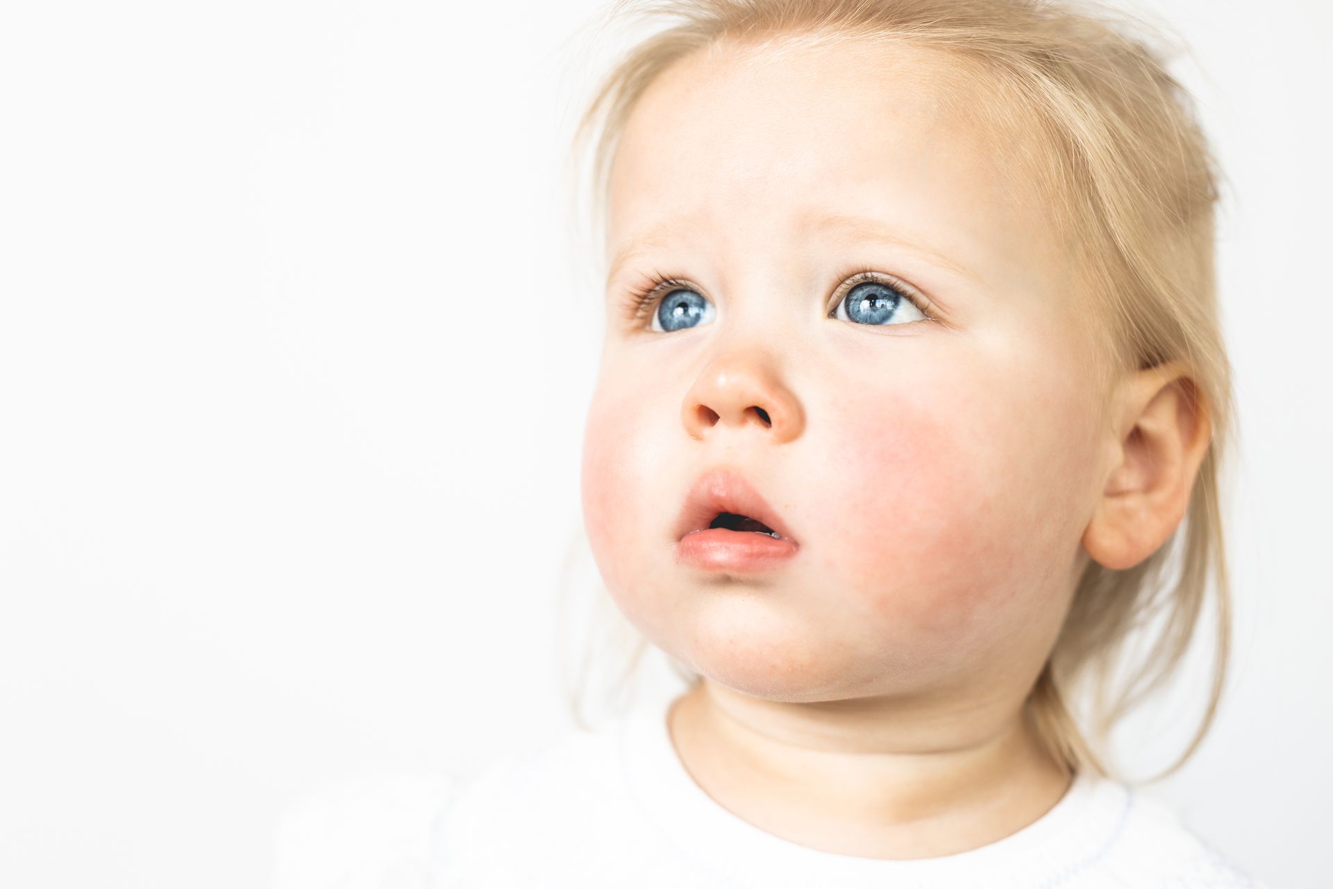 Blonde child with blue eyes looking upward against a white background