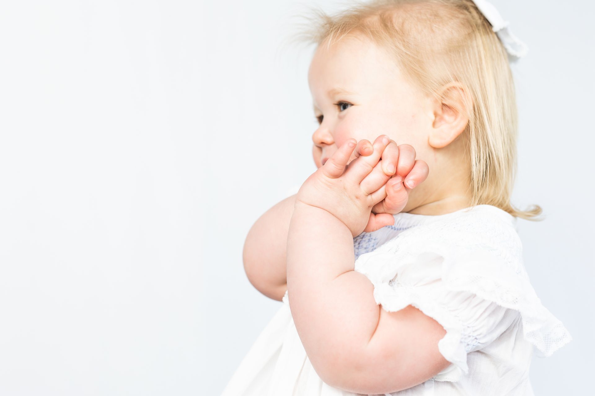 Smiling baby in a white dress touching their face against a light background