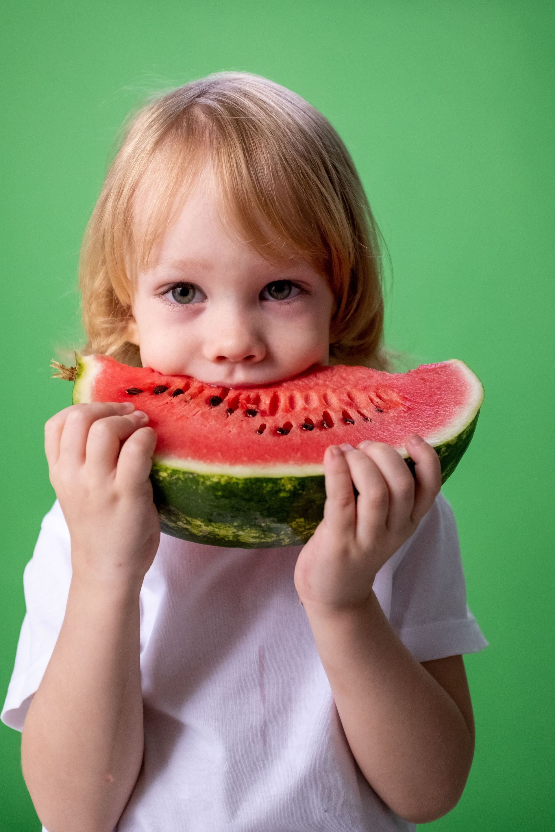 Child holding a large slice of watermelon against a green background