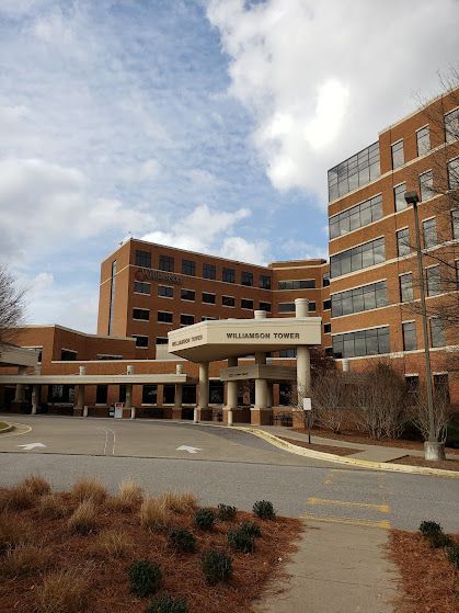 Entrance of a brick hospital or office building with a covered drop-off area and cloudy sky