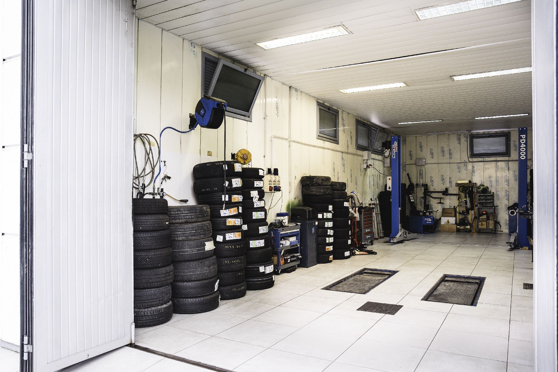 Interno di un'officina con pile di pneumatici, attrezzi e sollevatori per auto. Spazio luminoso, pulito e organizzato.