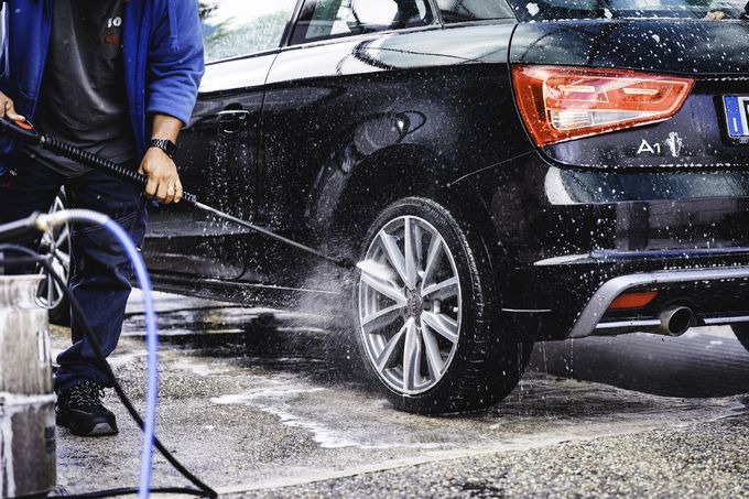 Persona che lava un'auto nera con un'idropulitrice; spruzzi d'acqua visibili autolavaggio Joel Milano