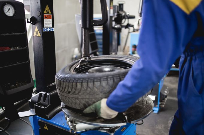 Un meccanico in tuta blu rimuove uno pneumatico dal cerchione con una macchina in un'officina.