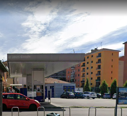 Una stazione di servizio con un'auto rossa e altri veicoli parcheggiati nelle vicinanze sotto un cielo nuvoloso.