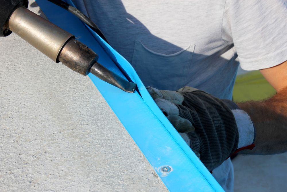 Close-up of a soldering iron tip touching a blue strap held by a gloved hand.