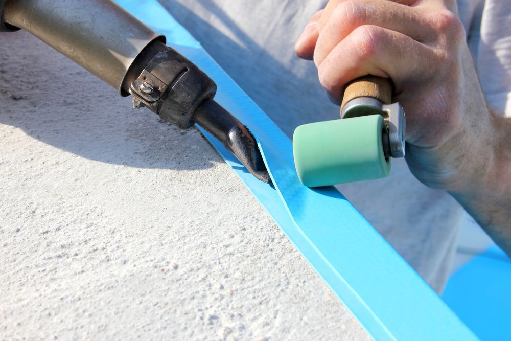 Hands painting a blue stripe on a textured wall with a roller and brush