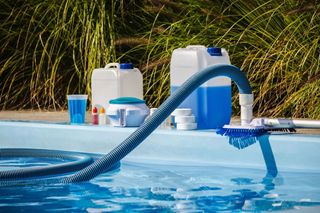 Pool cleaning supplies and hose beside a swimming pool with blue water and grass in the background