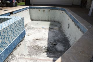 Empty concrete pool under repair, with chipped white walls and blue tile border.