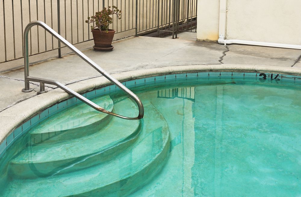 Curved pool steps with metal handrail beside turquoise swimming pool