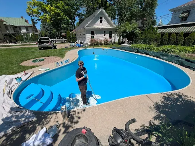 Person standing in a bright blue backyard pool with a white house and patio in the background