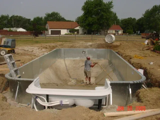 Empty in-ground pool under construction, with a worker standing inside and dirt piled around it.