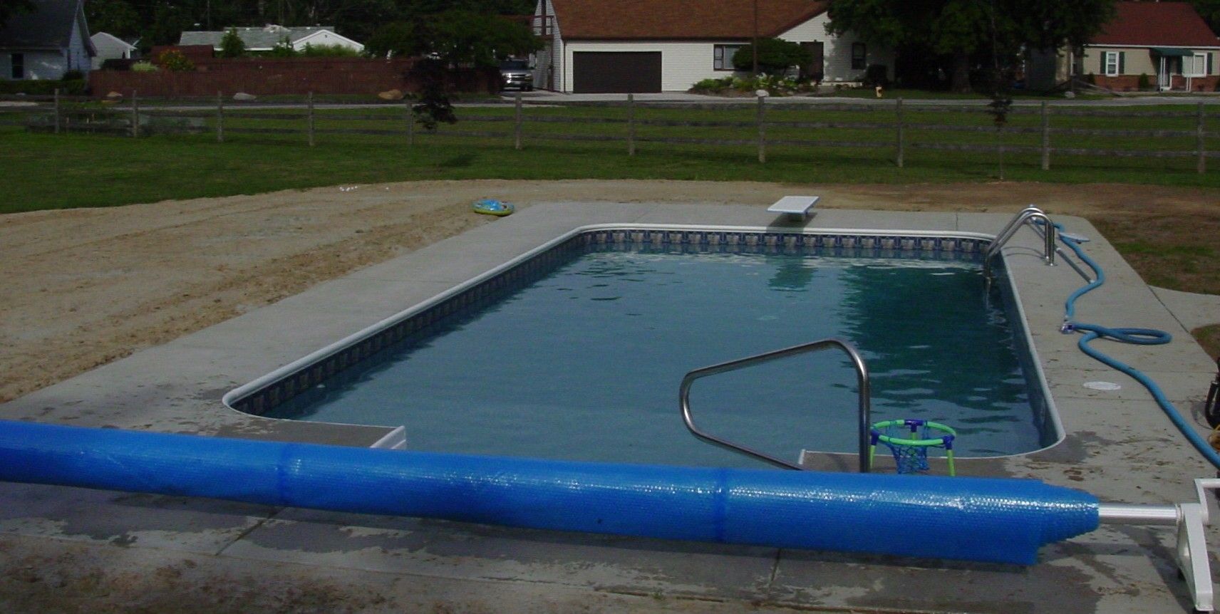 Outdoor swimming pool with a bright blue foam barrier across the foreground and a metal handrail at the steps.