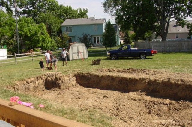Large dirt excavation in a backyard with a few people, a blue pickup truck, and a house in the background.