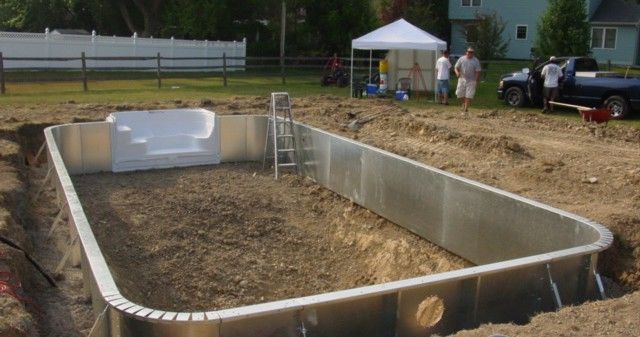 Empty backyard swimming pool under construction with white walls and workers in the background