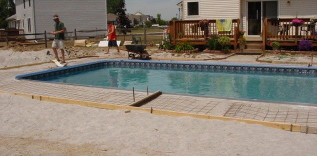 Outdoor motel pool with clear blue water, lounge chairs, and a small deck area beside a building.