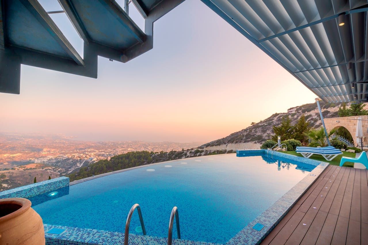 Infinity pool overlooking a city at sunset, with loungers and a covered terrace